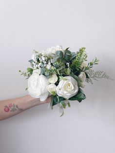 a person holding a bouquet of white flowers and greenery in their hand, against a wall