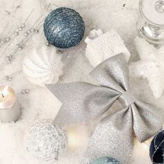 some ornaments are laying on the snow with one silver bow and two white balls in the background