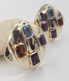 Title: Multicolor Gemstones Round Corner Square 14KT Yellow Gold Omega Clip Earrings Designer: Unbranded Material14KT Stamped Style: Vintage Gemstone Details All measurements are approximate and may vary slightly from the listed dimensions.1ar Approximately 5mm x 4mm each 1Amethyst Rectangular 1 Blue Topaz Rectangular 1 Orange Citrine Rectangular 1 Garnet Rectangular Estimated Measurements of the item30.23mm x 20.23mm x 5.83mm Estimated Total Weight of the Item DWT: 7.6 Grams: 11.7 Condition: Pr Luxury Multicolor Earrings For Evening, Luxury Multicolor Earrings With Gemstone Accents, Evening Multi-stone Round Earrings, Luxury Multi-stone Earrings For Anniversary, Luxury Multi-stone Gold Earrings, Luxury Multicolor Earrings For Formal Occasion, Luxury Multicolor Multi-stone Gemstones, Multicolor Gemstone Accented Fine Jewelry Earrings, Multicolor Gemstone-accented Fine Jewelry Earrings