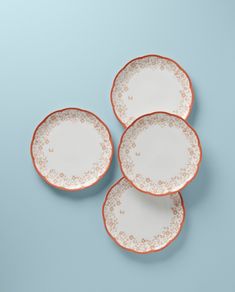 three white and orange plates sitting on top of a blue surface with gold trimmings