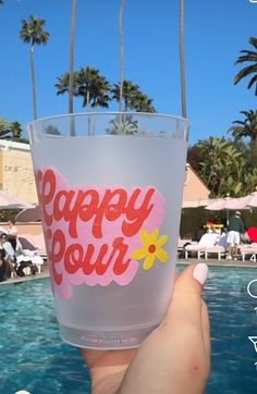 a person holding up a plastic cup with the words happy pour on it in front of a pool