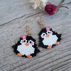 a pair of penguin beaded earrings sitting on top of a wooden table next to a flower