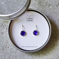 a pair of blue glass earrings sitting on top of a white box next to a mirror