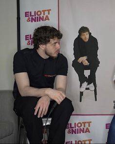 two men sitting next to each other in front of a poster