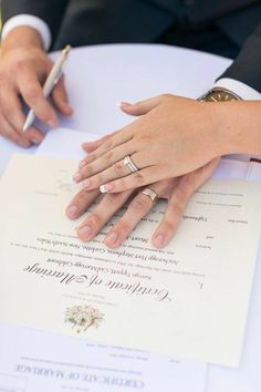 two people sitting at a table with wedding rings on their hands and papers in front of them