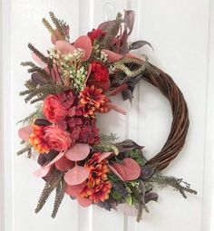 a wreath is hanging on the door with flowers and greenery in front of it