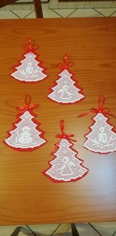 six christmas tree shaped doily on a wooden table with red ribbons and bows hanging from them