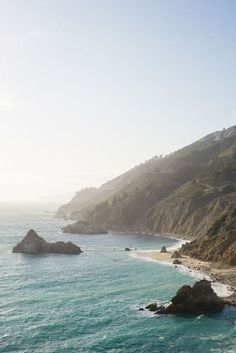 the ocean is blue and green as it passes by some hills with trees on them