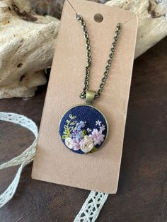 a necklace with flowers on it sitting next to a piece of lace and a tag