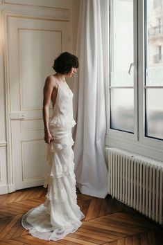 a woman in a white dress standing next to a window