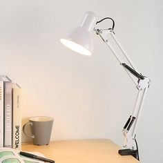 a desk lamp sitting on top of a wooden table next to books and a cup