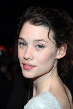 the face of a woman with blue eyes and brown hair, wearing a white dress