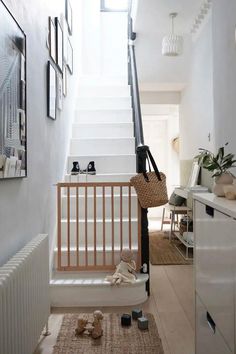 Bright Scandinavian-inspired hallway with a black and white staircase, baby gate, and minimalist decor. Features a woven rug, children's toys, and a basket hanging on the stair rail. The white walls, natural light, and simple accents create a warm, family-friendly entryway. Stair Gate Ideas, Wooden Stair Gate, Stairs Gate, Wooden Baby Gates, Scandinavian Hallway, Minimalist Hallway, Bauhaus Interior, White Worktop, Home With Kids