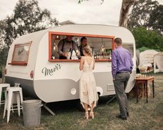 a man and woman are standing in front of a camper that is parked on the grass