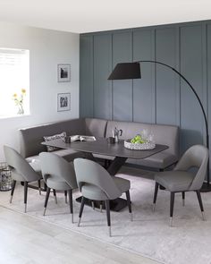 a corner table with grey chairs and a black lamp in a room that has gray paneling on the walls