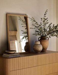 a vase with some plants on top of a dresser next to a mirror and a bowl