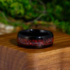 a black ring with red speckles sitting on top of a wooden table next to some bushes