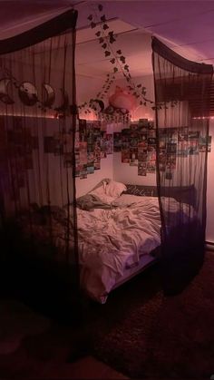 an unmade bed in a room with pictures hanging on the wall and curtains over it