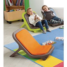 two children sitting on chairs in a room with colorful rugs and bookshelves