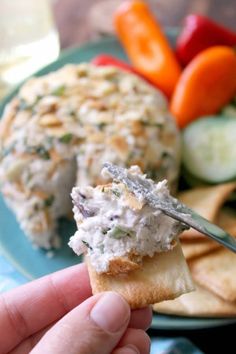 a hand holding a cracker with chicken salad on it and vegetables in the background