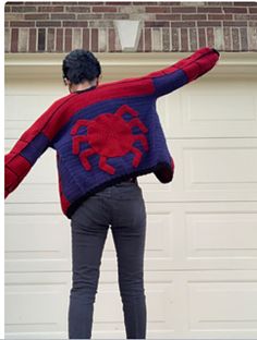 a person wearing a spiderman sweater standing in front of a garage door with their arms outstretched