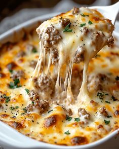 a spoon full of cheese and meat casserole being lifted from the casserole dish