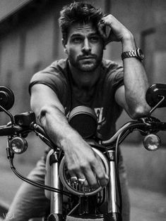 a black and white photo of a man sitting on a motorcycle with his hand on the handlebars