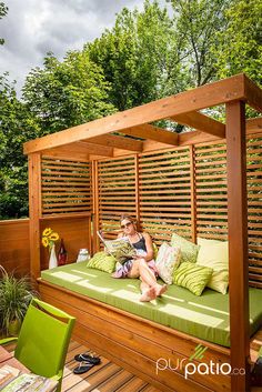 a woman sitting on top of a green couch under a wooden pergolan bed