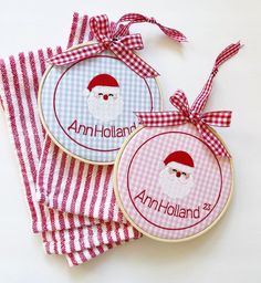 two cross stitch christmas coasters with santa's face and name on the front