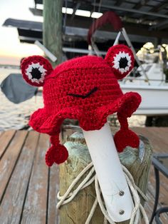 a red crocheted hat with an eyeball on it sitting on top of a piece of wood