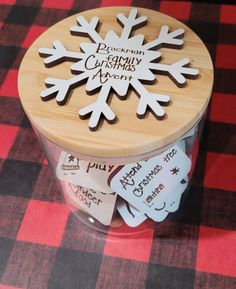 wooden snowflake cutouts are displayed in a jar on a red and black checkered tablecloth