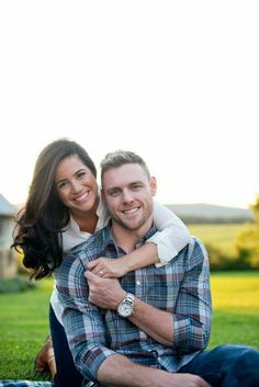 a man and woman are sitting on the grass in front of a house with their arms around each other