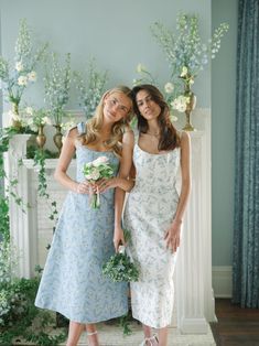 two beautiful young women standing next to each other in front of a fireplace with flowers