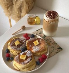 pancakes with butter and berries on a plate next to a cup of coffee, honey shake