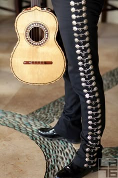 a person holding an acoustic guitar in their right hand and wearing black shoes on the other side