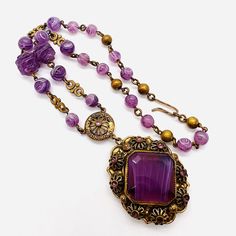 "Gorgeous vintage WEST GERMANY purple slag glass beaded necklace. Ornate gilt metal set with center purple slag glass stone surrounded by flowerette settings with amethyst rhinestones and on purple slag glass beaded necklace. Pendant measures 2 5/8 inches tall at the heart and 1 1/2 inches wide. The glass beaded chain is 3/8 inch wide at widest point. Total length is 17 inches long. Signed \"West Germany\" on hook clasp. Hook and dangle clasp secure. Excellent vintage condition with minimal age Handmade Antique Purple Jewelry, Antique Handmade Purple Jewelry, Purple Beaded Vintage Necklace, Purple Vintage Beaded Necklace, Vintage Purple Beaded Necklace, Vintage Natural Stones Beaded Necklaces, Vintage Beaded Necklaces With Natural Stones, Vintage Amethyst Cabochon Jewelry, Vintage Purple Amethyst Jewelry