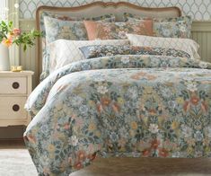 a bed with floral comforter and pillows on top of it in a room next to a dresser