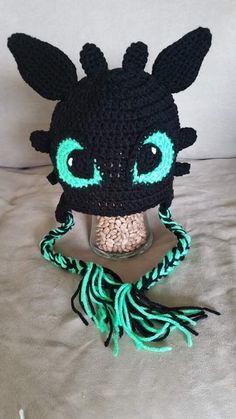 a crocheted black and green hat with blue eyes on top of a bed