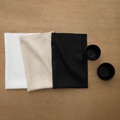 three black and white napkins sitting on top of a wooden table next to cups