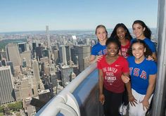 four girls in red and blue shirts standing on top of a building looking at the camera