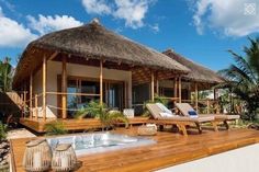 an outdoor hot tub sitting on top of a wooden deck next to a building with thatched roof