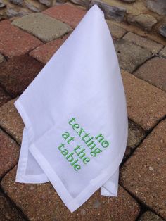 a white napkin with green lettering on it sitting on top of a brick floor next to a stone wall