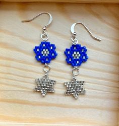 These mini Stars of David dangling from beautiful blue and silver flowers are fresh and modern Jewish symbol earrings.  Hand-beaded using Miyuki Delica beads, these earrings are delicate and sweet. Completed with sterling silver ear wires, they are comfortable and secure. Enjoy the attention! Length: 1.25" Blue Sterling Silver Earrings With Flower Charm, Blue Flower Sterling Silver Earrings, Blue Flower-shaped Sterling Silver Earrings, Hypoallergenic Blue Star Earrings, Handmade Silver Dangle Flower Earrings, Silver Minimalist Beaded Earrings, Handmade Blue Sterling Silver Flower Earrings, Blue Sterling Silver Earrings With Silver Beads, Silver Star-shaped Beaded Earrings