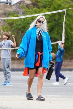 a woman in blue jacket and orange skirt walking on street with other people behind her