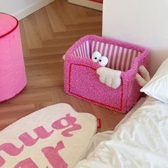 a pink dog bed next to a stuffed animal in a pink box on the floor