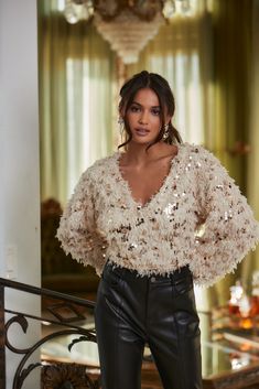 a woman standing in front of a chandelier wearing black pants and a white top