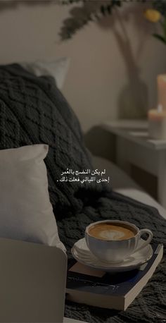 a cup of coffee sitting on top of a bed next to a book and candle