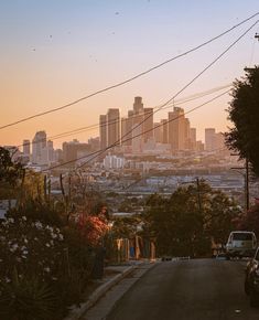 the sun is setting over a city with power lines in the foreground and cars parked on the street