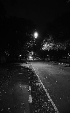 an empty street at night with no cars on the road and trees in the background