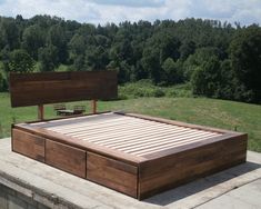 a wooden bed frame sitting on top of a cement slab next to a lush green field